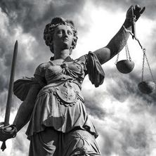 Justitia in schwarz-weiß vor bedrohlichen Wolken