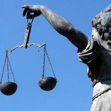Justitia mit Wage in der Hand von schräg hinten vor blauem Himmel