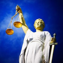 weiße Justitia mit Wage und Schwert vor blauem Himmel