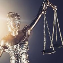Justitia mit gehobenem Arm im Gegenlicht, in der Hand hält sie eine Wage